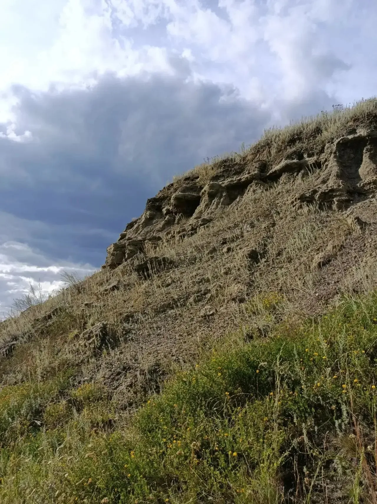 Обрыв со слоистой породой древнего морского дна под облаками